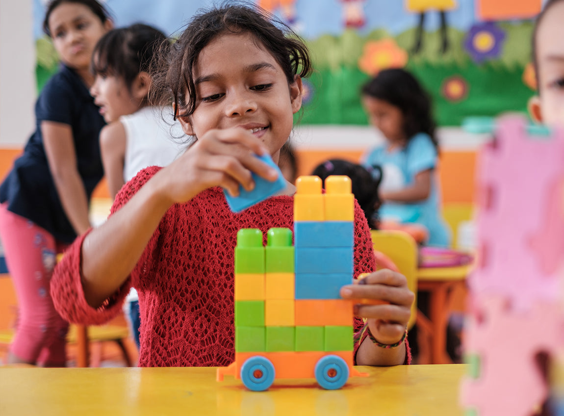 Une jeune fille empile des blocs colorés dans une salle de classe.