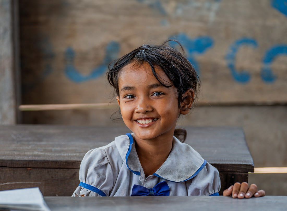 Une petite fille portant un uniforme scolaire est assise à son bureau et sourit.