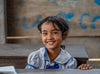 Une petite fille portant un uniforme scolaire est assise à son bureau et sourit.