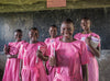 Cinq jeunes filles en uniforme rose se tiennent devant un tableau noir. Chacune a un livre dans les bras.