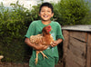  Un jeune garçon souriant portant un T-shirt vert tient une poule dans ses bras.