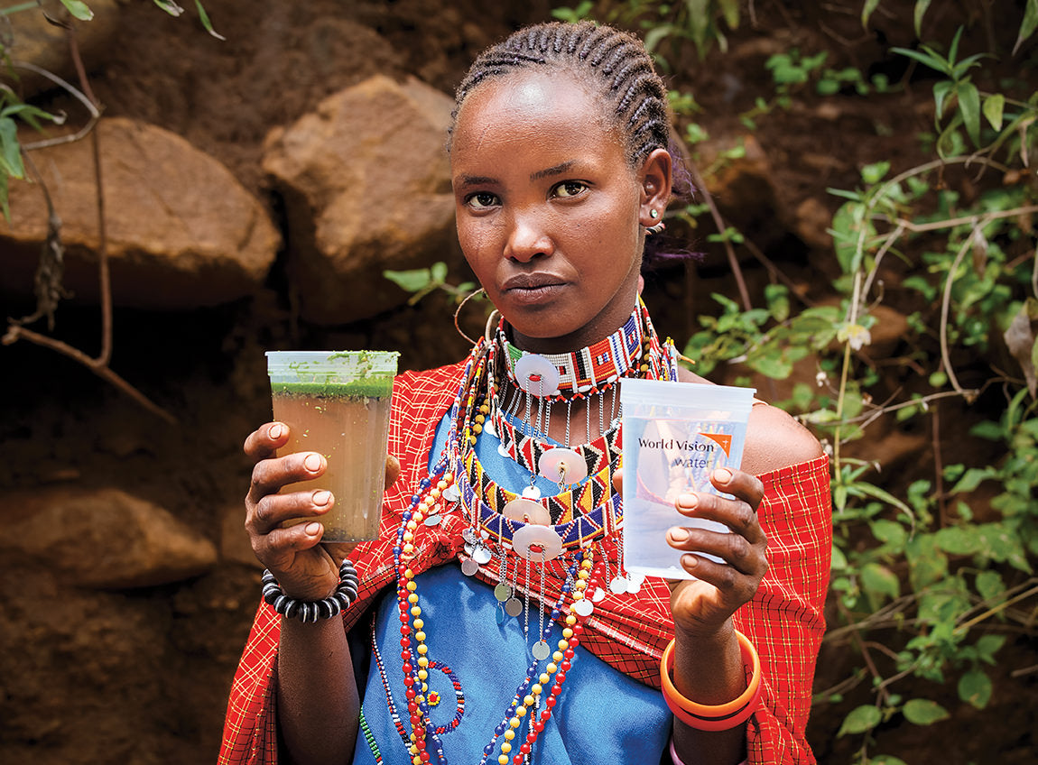 Une femme en tenue africaine tient un gobelet d’eau sale dans la main droite et un gobelet d’eau potable dans la main gauche.