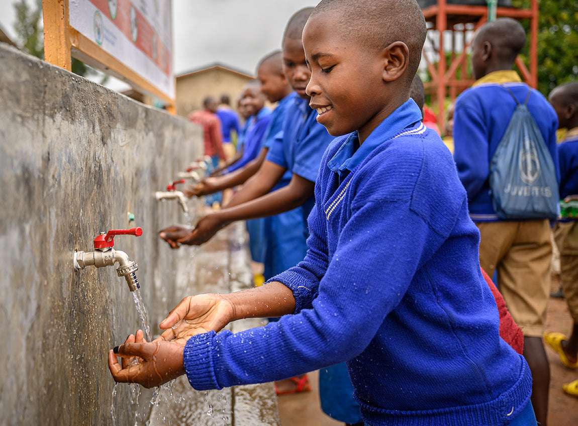Des écoliers portant des chandails bleus lavent leurs mains grâce à des robinets collectifs.