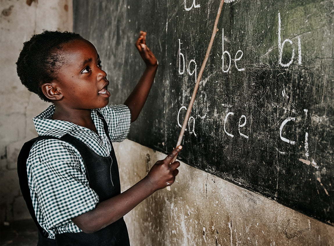 Une jeune fille pointe l’alphabet inscrit sur le tableau d’une salle de classe.