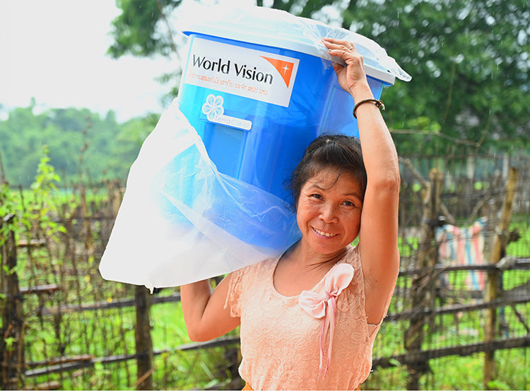 Une femme sourit en levant un filtre à eau fourni par Vision Mondiale.