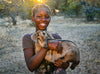 Une jeune fille souriante est debout, dehors, avec une chèvre dans les bras.