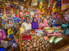 Un homme et deux femmes sourient. Ils se tiennent dans un magasin qu’ils gèrent, rempli de divers biens et fruits et légumes.