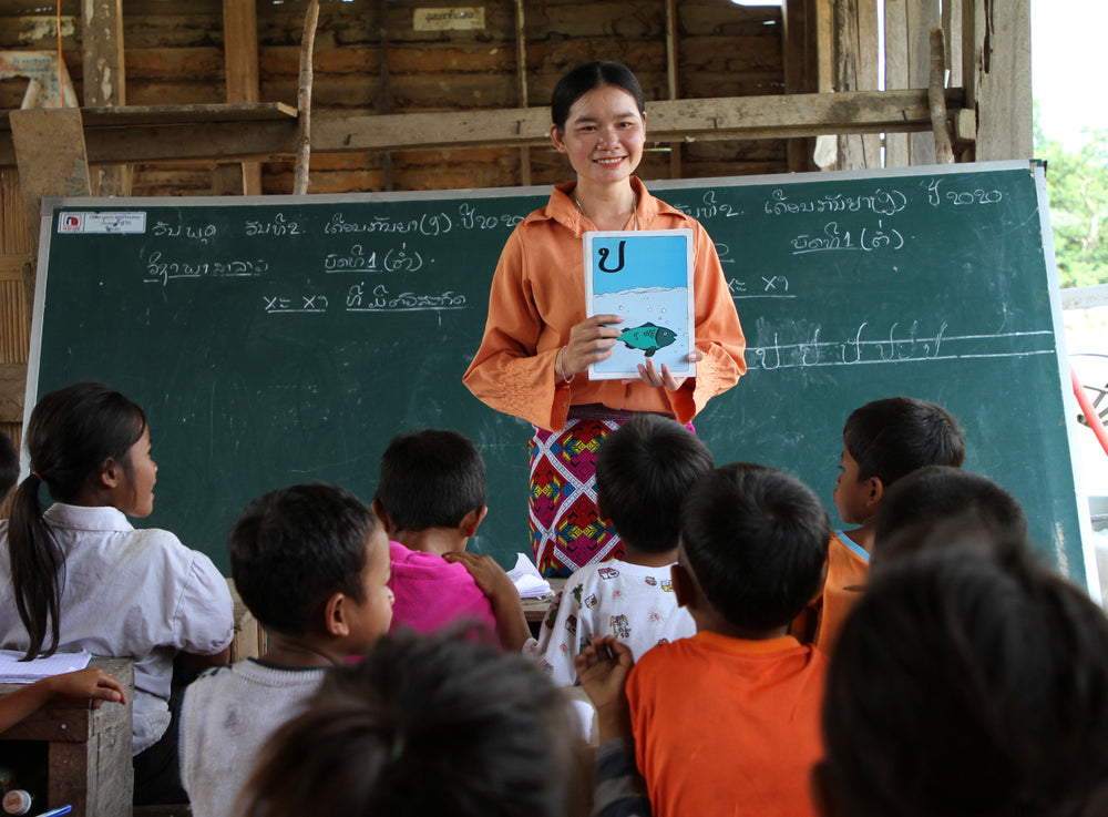 Une femme se tient devant un tableau et présente un livre aux enfants dans la salle de classe.