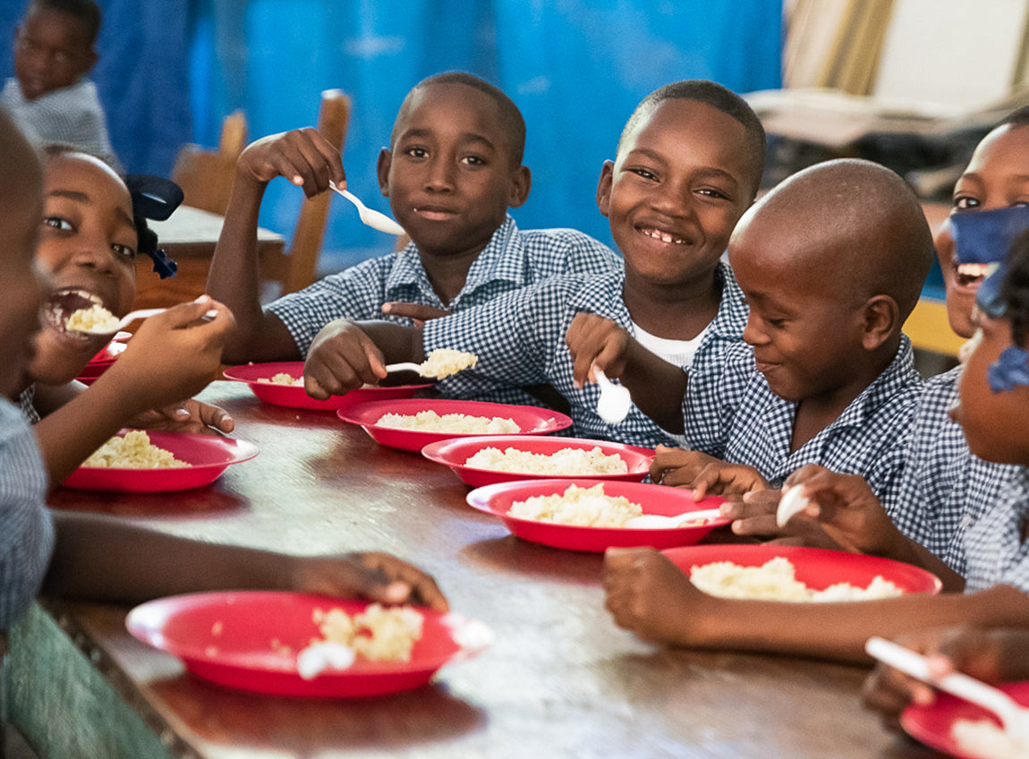 Un groupe d’écoliers sourient pour la photo tout en savourant leur repas.
