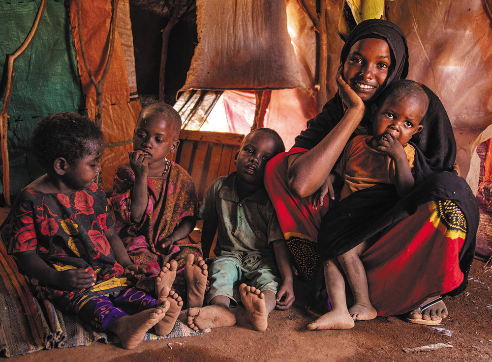Une femme et ses quatre enfants sont assis dans une tente remplie de tissus.