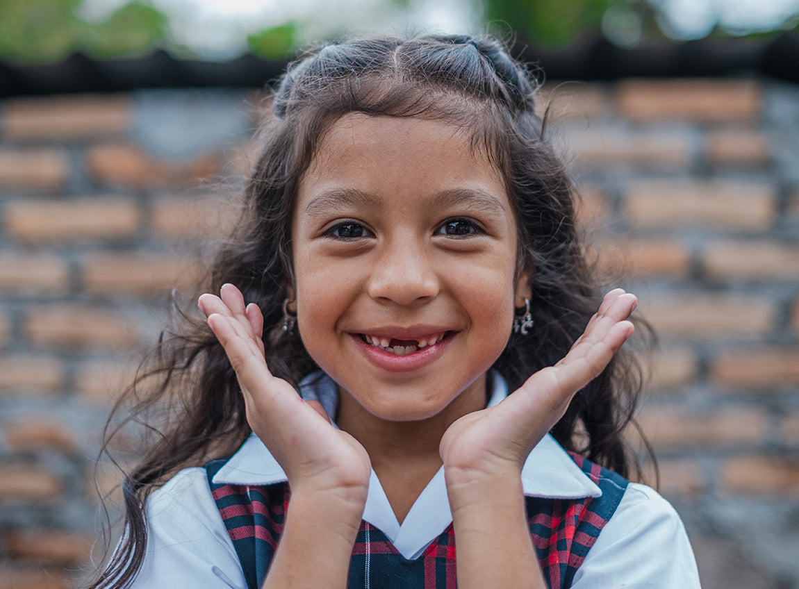 Une jeune fille fait un sourire pour la photo, ses mains encadrant son visage.