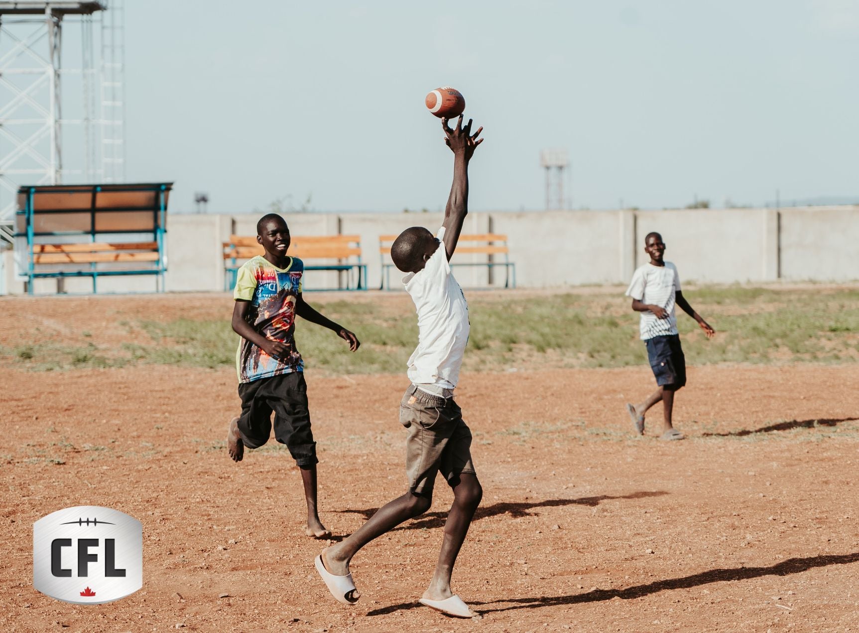 Des enfants jouant avec enthousiasme tendent les mains vers un ballon de football. Le logo de la Ligue canadienne de football est superposé dans le coin inférieur gauche de l'image.