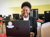 Une jeune fille assise dans une salle d’informatique utilise l’ordinateur devant elle en souriant pour la photo.