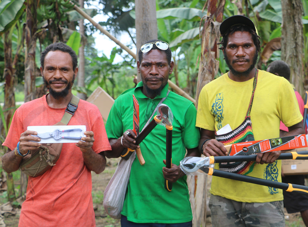 Trois hommes sont debout devant une forêt, divers outils de paysagisme entre les mains.