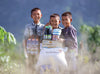Sourire aux lèvres, trois garçons se tiennent côte à côte derrière une pile de produits alimentaires.