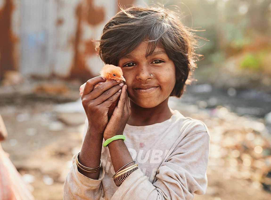 Tournée vers l’objectif, une petite fille tient un poussin dans ses mains.