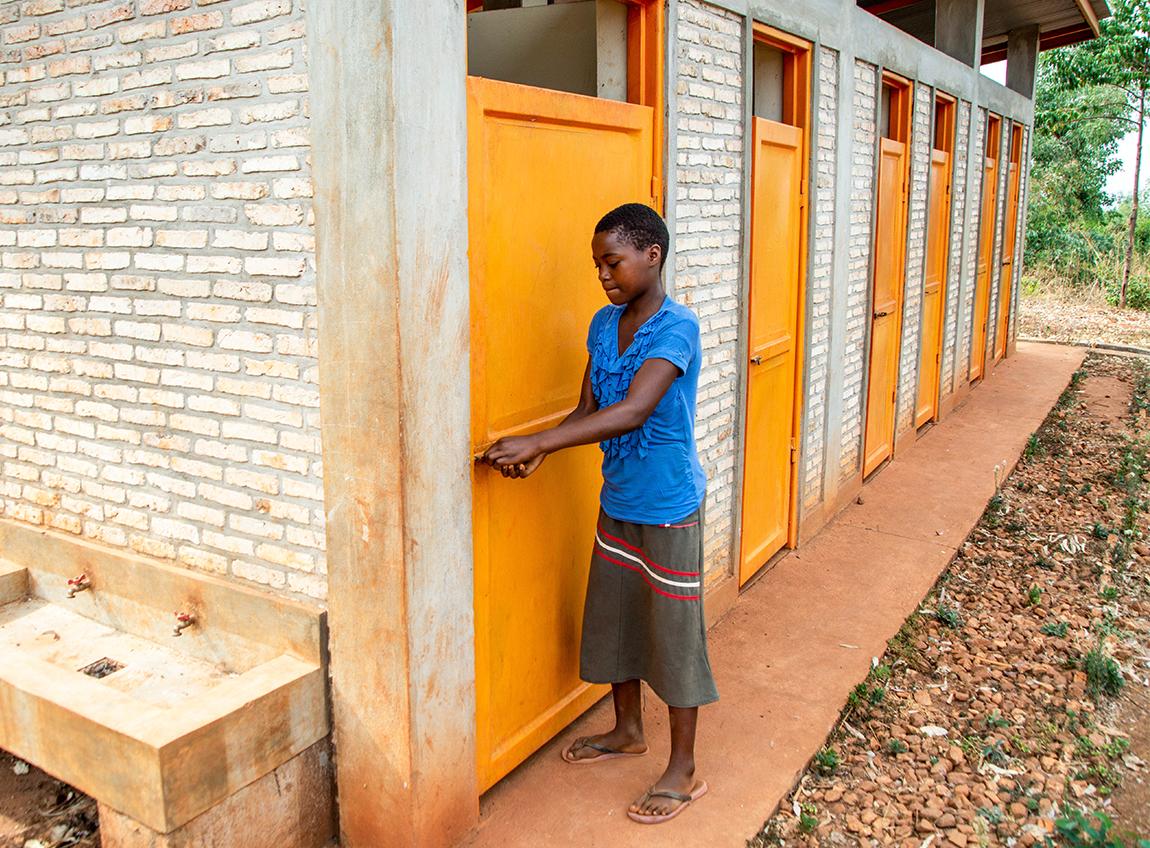 Une fille portant une jupe et un haut bleu ferme la porte d’une cabine de toilettes.
