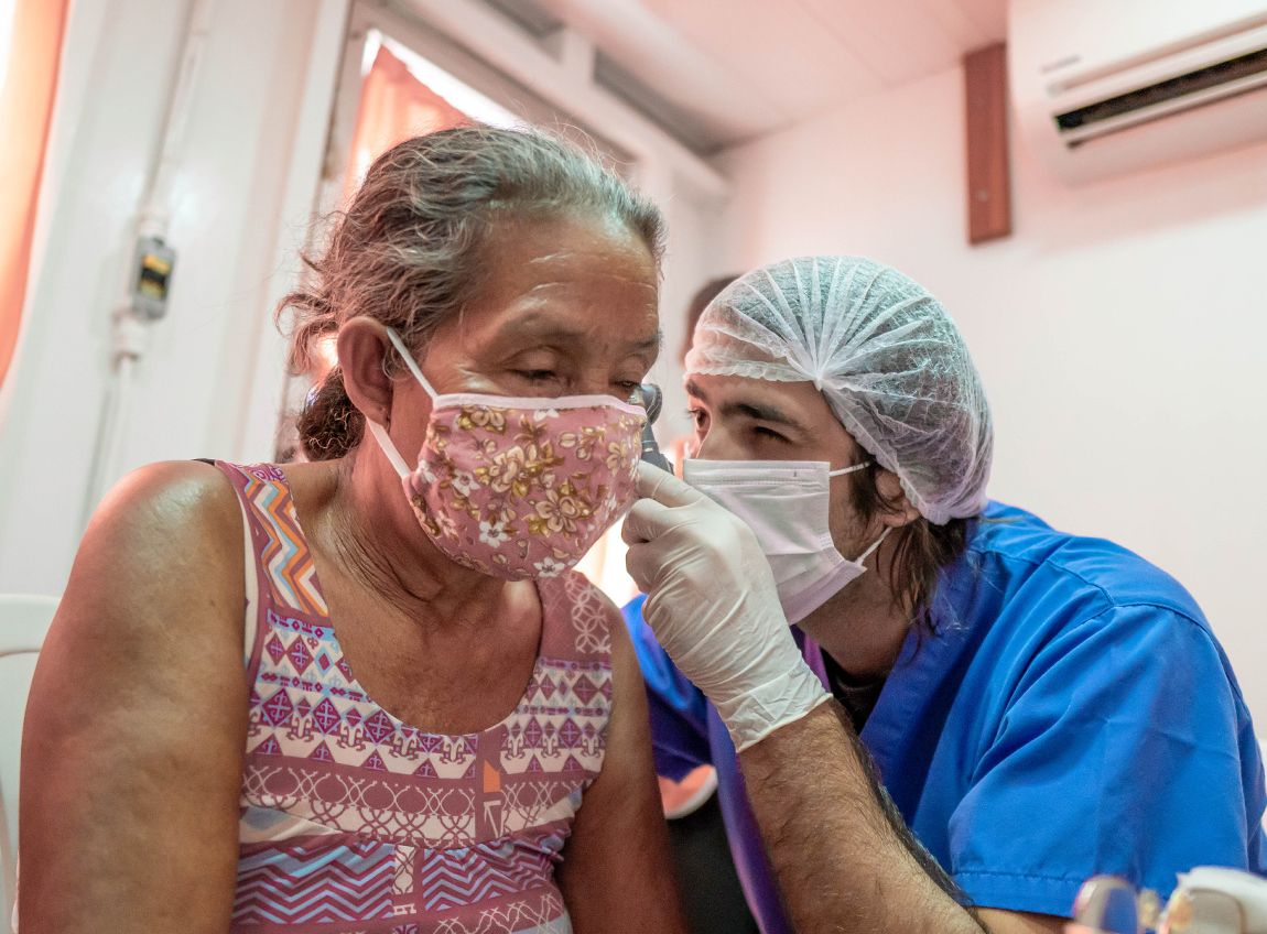 Un professionnel de la santé portant un masque, des gants et un filet de protection pour cheveux, examine l’oreille d’une patiente, portant également un masque.