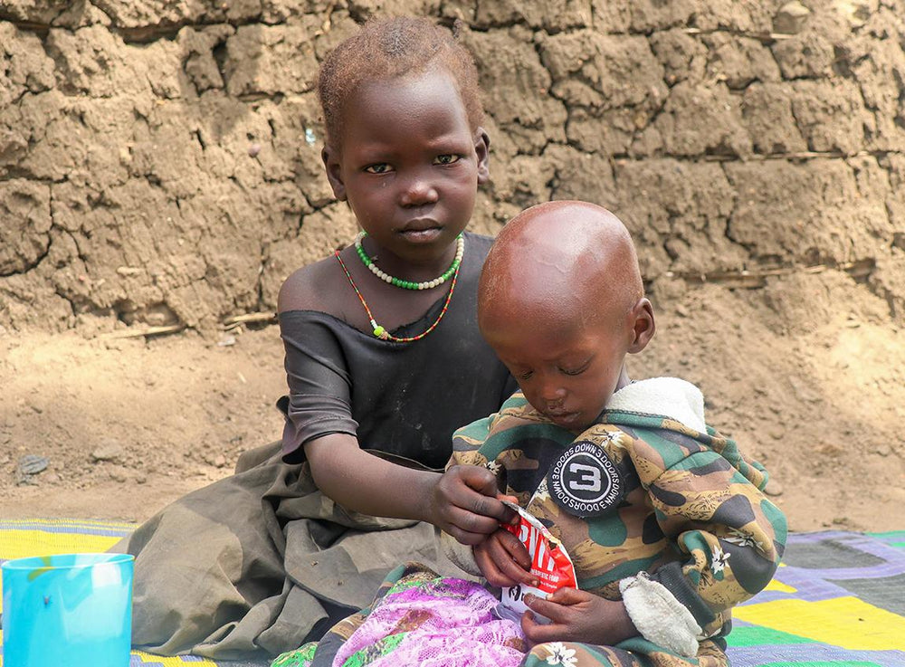 Deux très jeunes enfants affectés par la faim sont assis par terre.