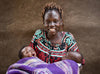 Une femme sourit vers l’objectif en tenant deux nouveau-nés enveloppés dans une couverture mauve.
