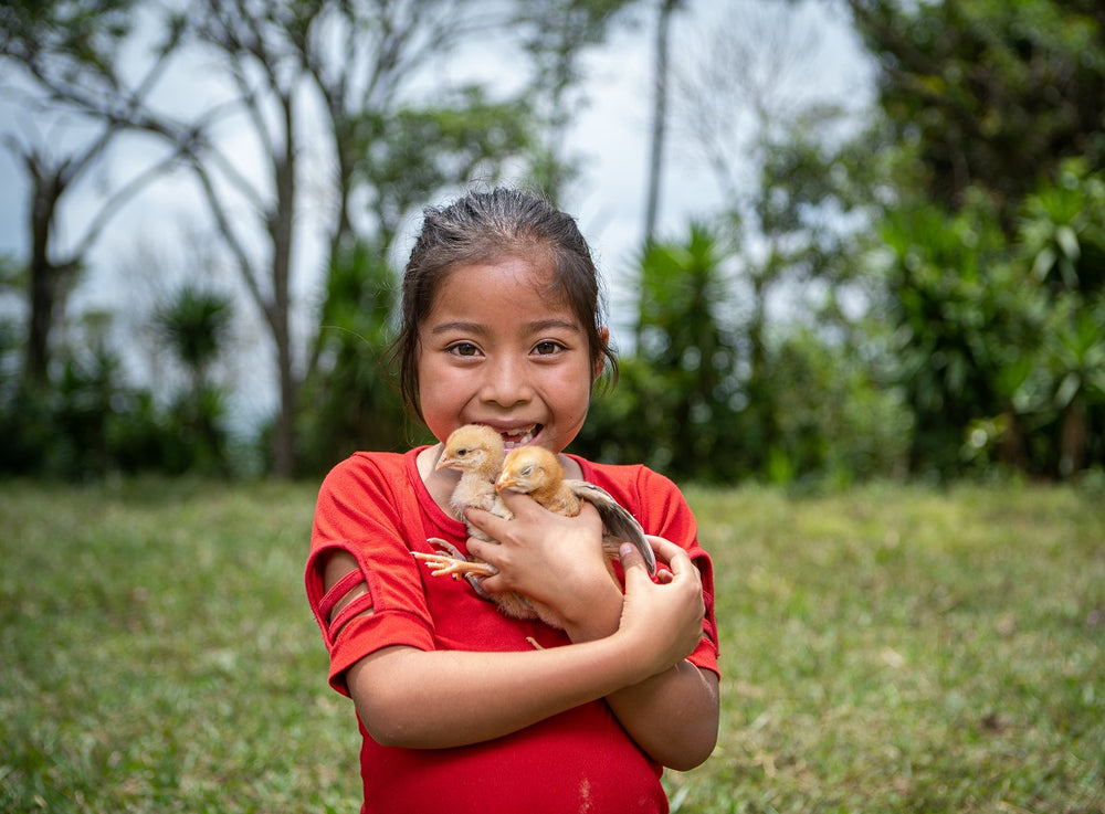 Une petite fille sourit tout en tenant deux poussins devant l’objectif.