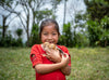 Une petite fille sourit tout en tenant deux poussins devant l’objectif.