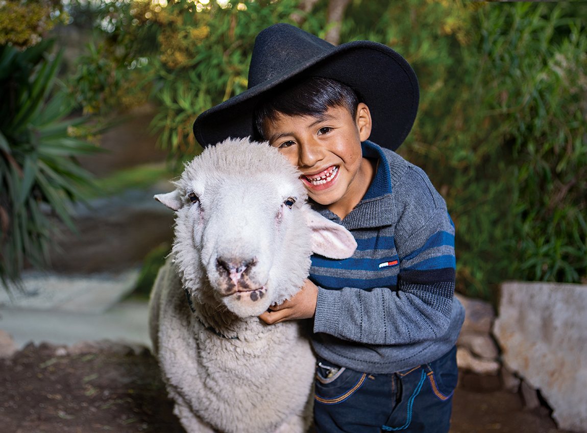  Un jeune garçon souriant portant un chapeau de cow-boy noir et prend un mouton dans ses bras.