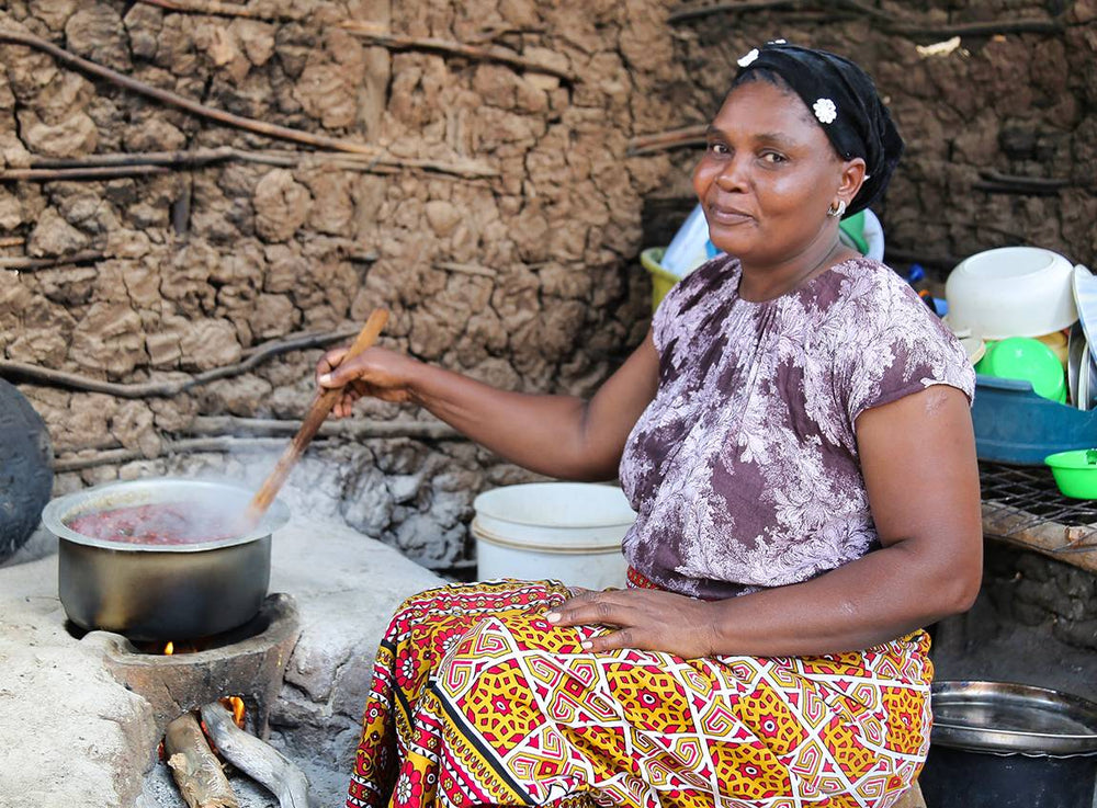 Entourée de pots et de bols, une femme assise remue le plat avec une cuillère en bois. 
